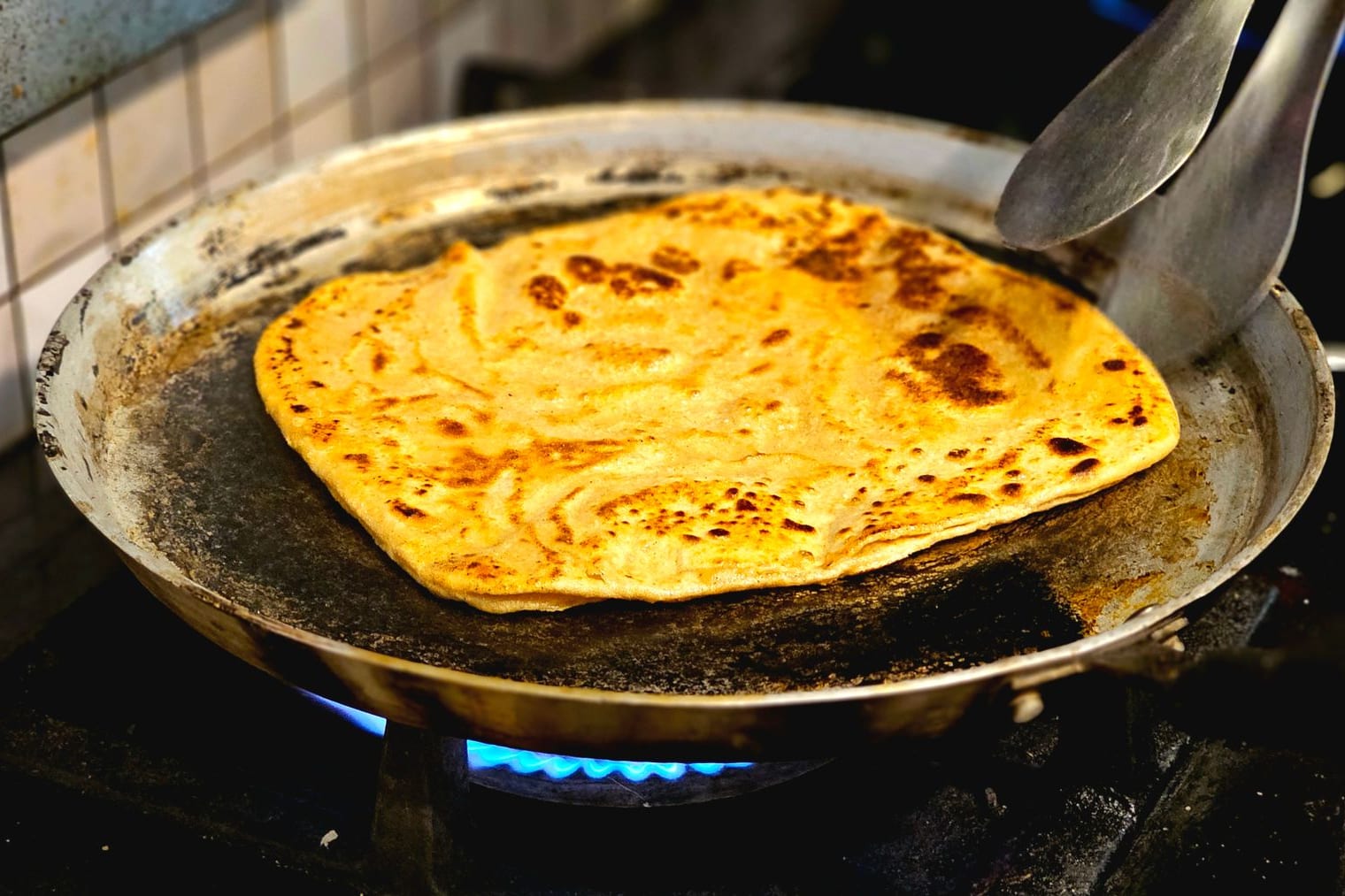 Stuffed kulcha browning on a griddle at a Punjab breakfast counter